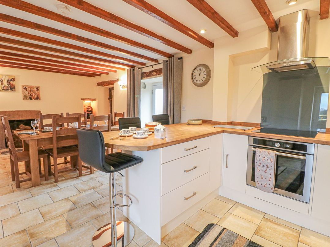 A kitchen with a wooden countertop, stove, and bar stool next to a dining area with a wooden table and chairs at Lane Head Cottage in Alderwasley near Wirksworth