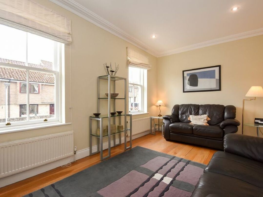A living room with black leather sofas glass shelving and large windows at Churchside in Alnwick
