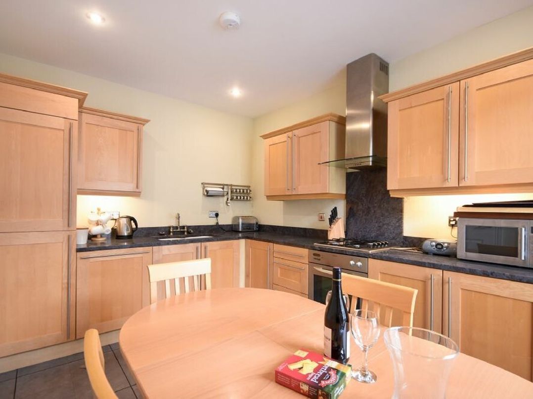 A kitchen with wooden cabinets a round dining table with a bottle glass and a box on it at Churchside in Alnwick
