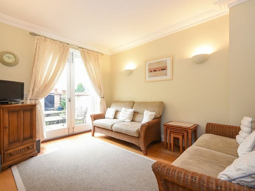 A sitting room with two sofas a wooden cabinet and glass doors with curtains at Churchside in Alnwick