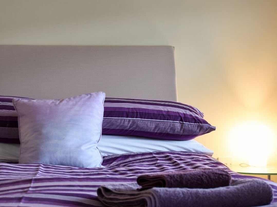 A bed with purple striped bedding white pillow and folded towels on top at Churchside in Alnwick