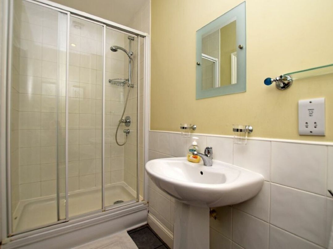 A bathroom with a shower enclosure and a pedestal sink with a mirror above at Churchside in Alnwick
