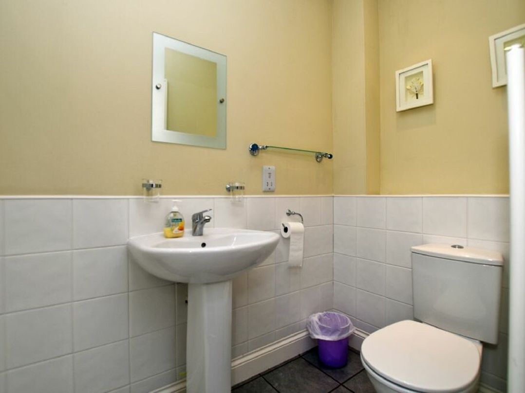 A bathroom with a sink a mirror a toilet and a small trash bin at Churchside in Alnwick