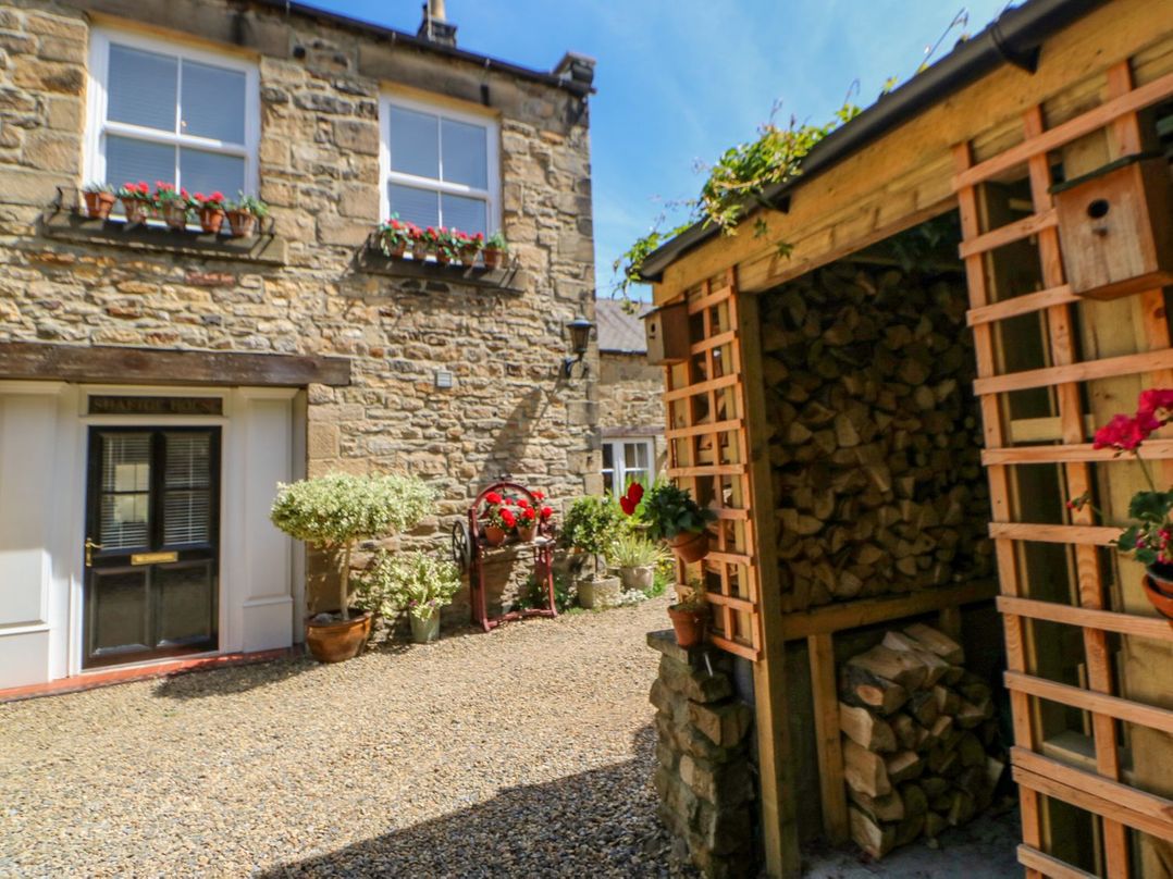 A courtyard with stacked firewood a stone house flower pots and gravel ground at Shaftoe Mews in Haydon Bridge