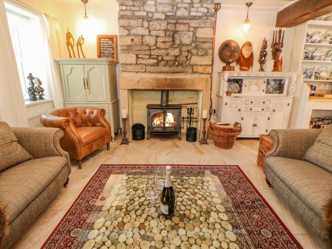 A living room with a stone fireplace leather and fabric sofas a glass coffee table with wine bottle and glasses at Shaftoe Mews in Haydon Bridge