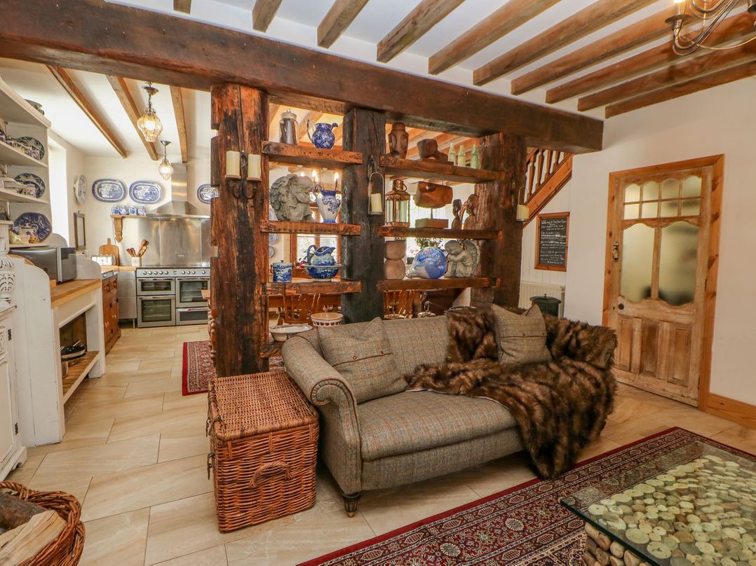 A living area with a sofa, wooden shelves holding pottery and sculptures, kitchen with appliances, and a wooden door at Shaftoe Mews in Haydon Bridge