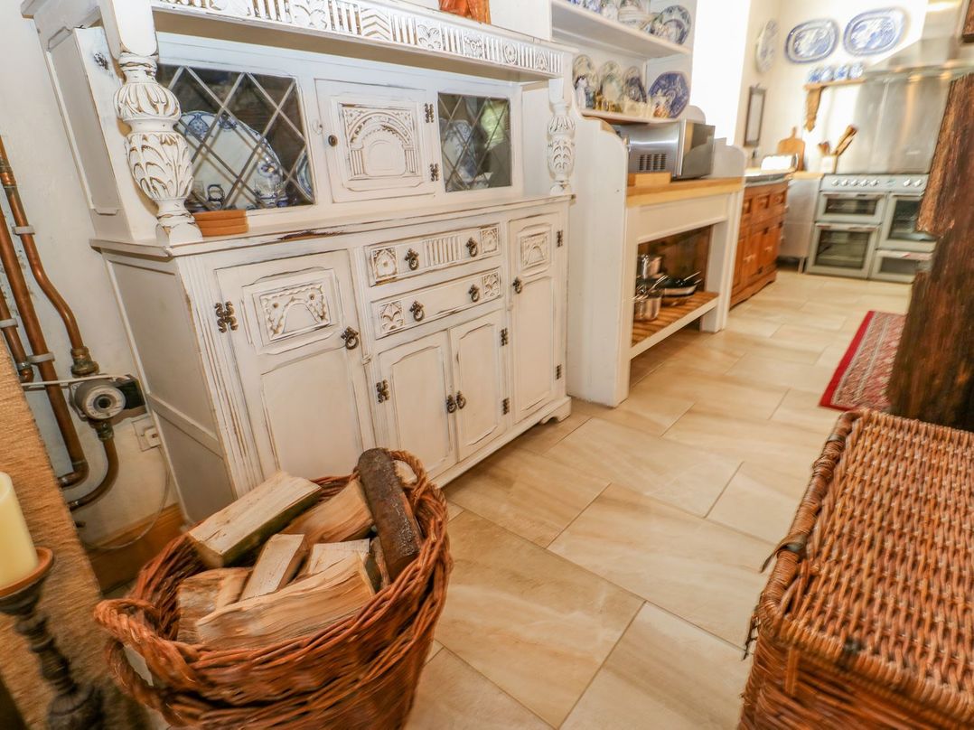 A kitchen with a white vintage cabinet a basket of firewood tile flooring and a wicker storage box at Shaftoe Mews in Haydon Bridge