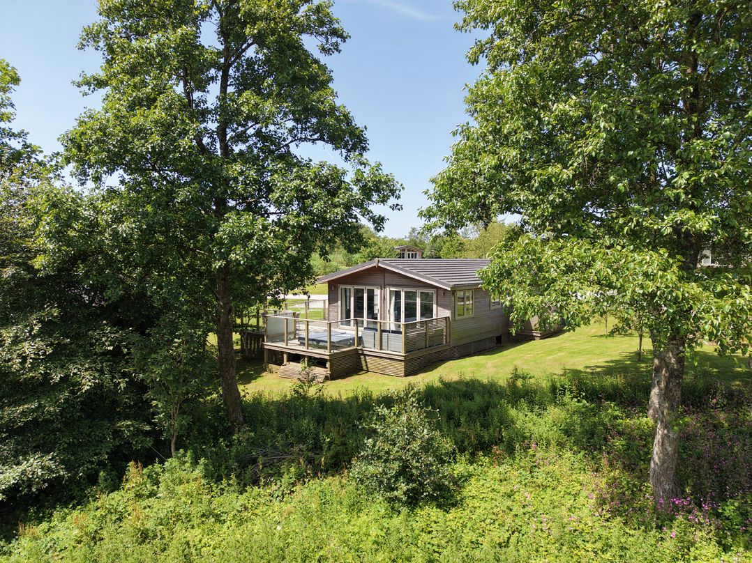 A cabin with a deck surrounded by trees at 20 Meadow Retreat in Dobwalls