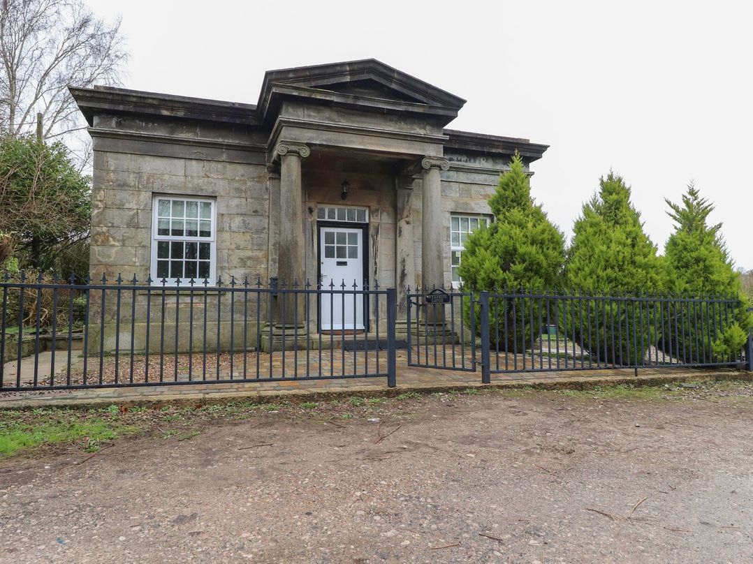 A building with a fence and trees at The Lodge House in Dolphinholme near Galgate