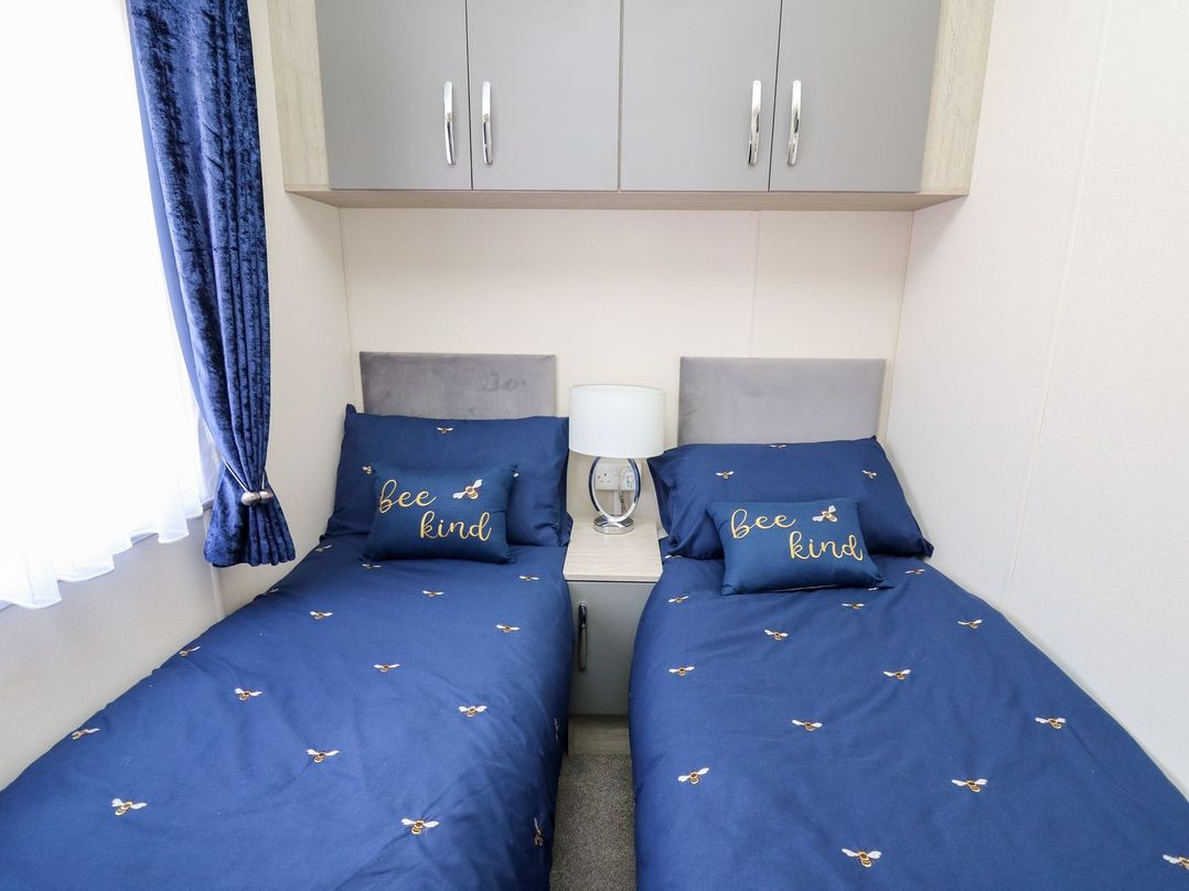 A bedroom with two beds and a bedside table at 33 Woodpecker Lodge Llanarth