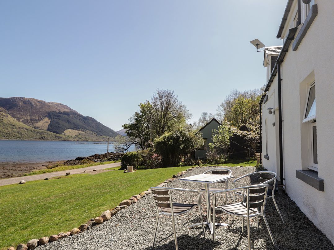 A patio with a table and chairs facing a lake and mountains at Tigh a Phailean in Letterfearn
