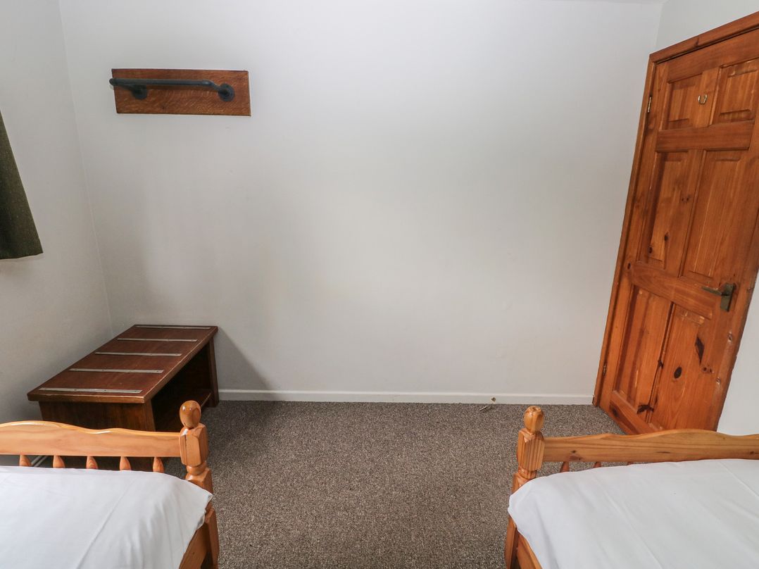 A bedroom with two beds, a door, a bench, and a wall shelf at Cabin No. 9 - Salt and Fern Cabins Goytre near Port Talbot