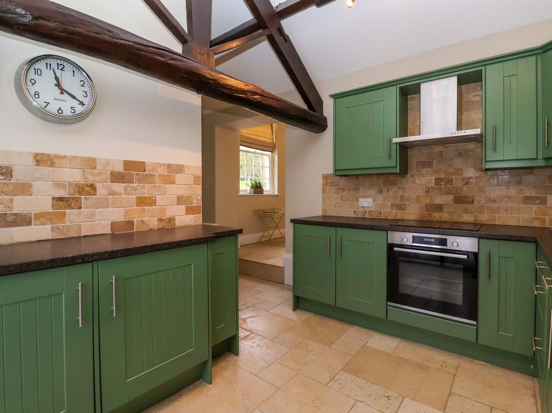 A kitchen with green cabinets and a clock at The Bothy in Knaresborough