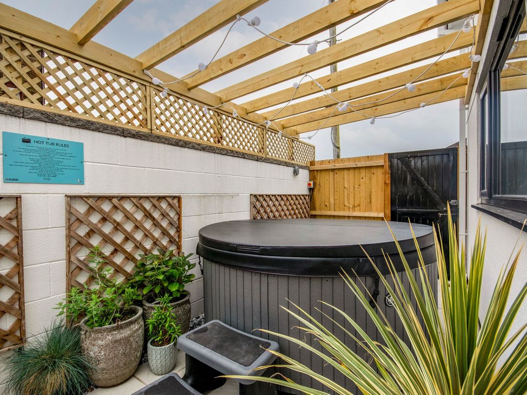 An outdoor patio with a hot tub and surrounding plants at Seagull Shack in Morfa Bychan