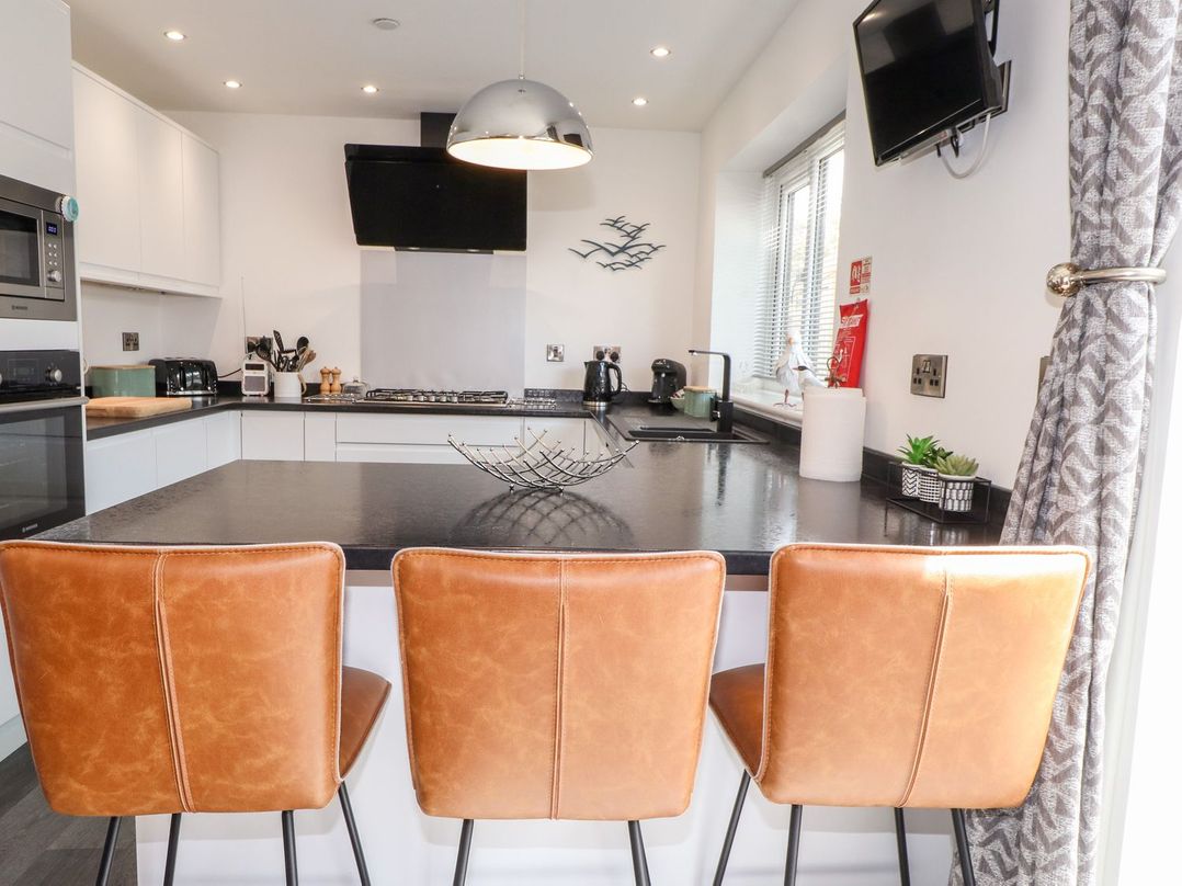 A kitchen with bar stools and appliances at Seagull Shack in Morfa Bychan