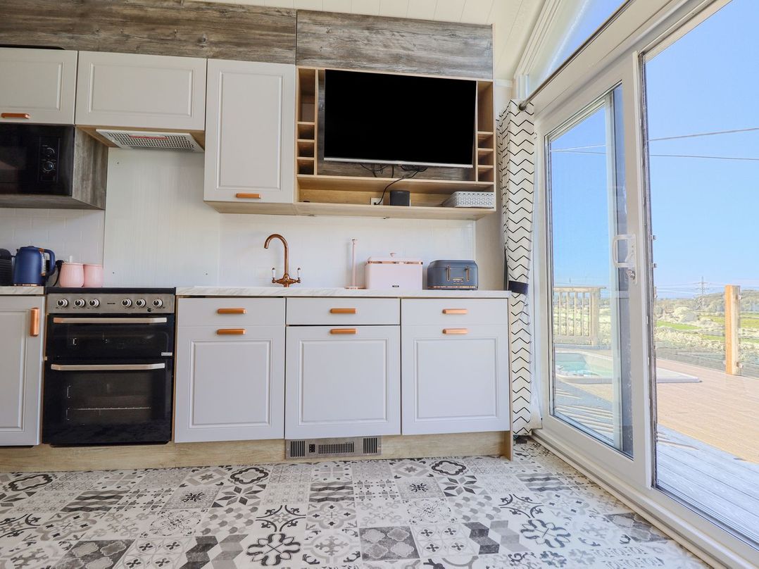 A kitchen with cabinets, oven, and TV at Posh Pod in Cemaes Bay