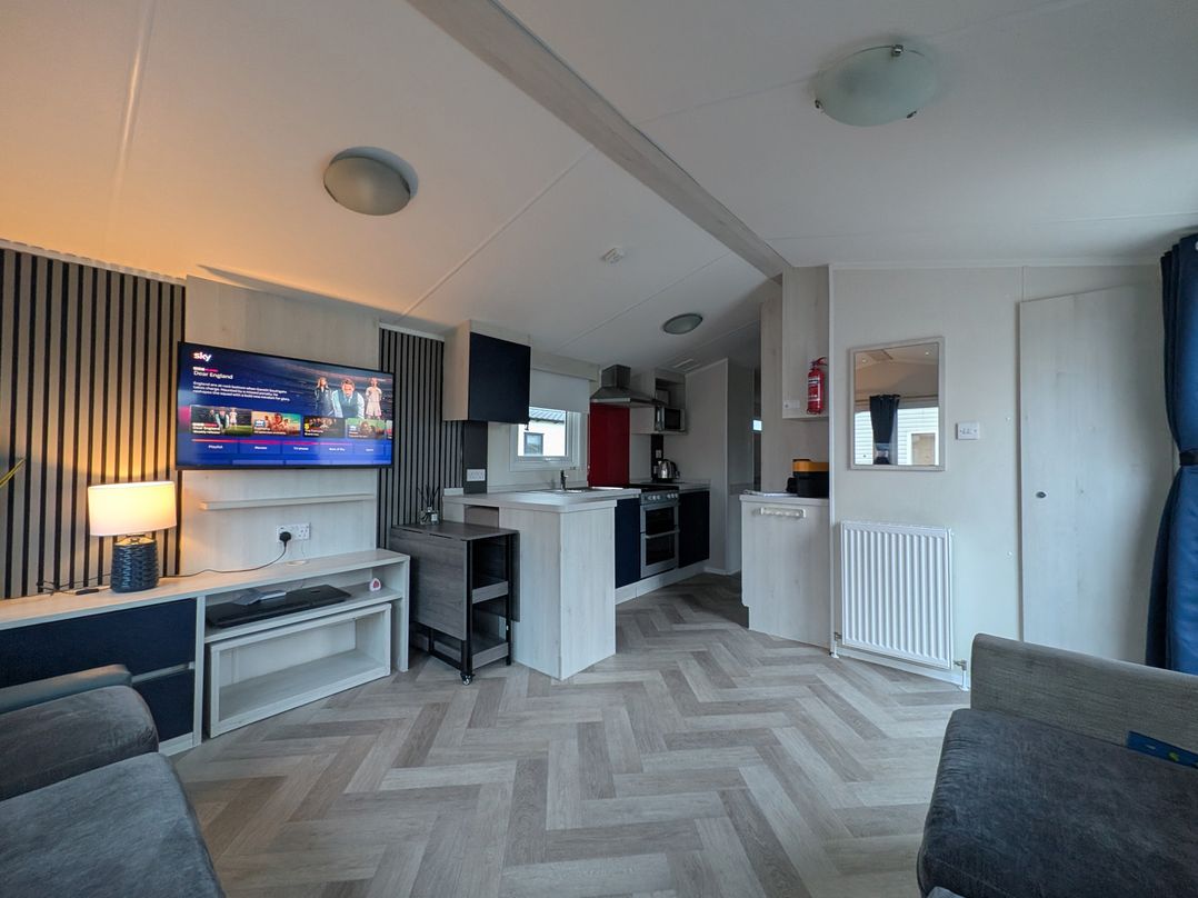 A living room with a tv and kitchen area at Presthaven - Denbigh Dunes in Gronant