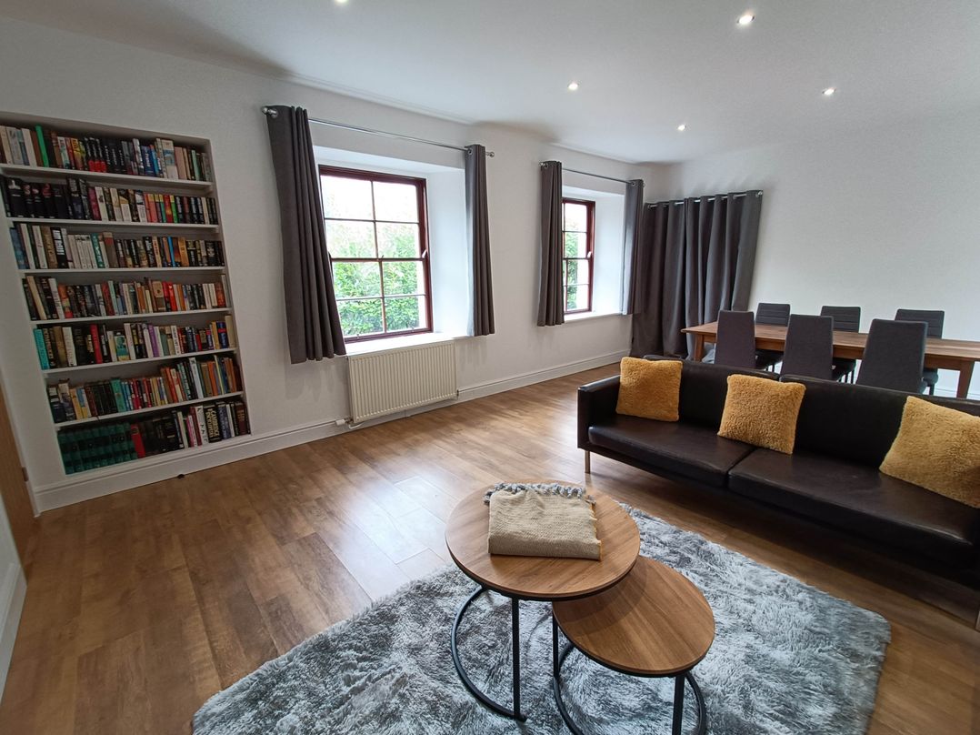 A living room with a bookshelf, sofa, dining table, and window at RnB Rural n Beautiful Near Barrhill