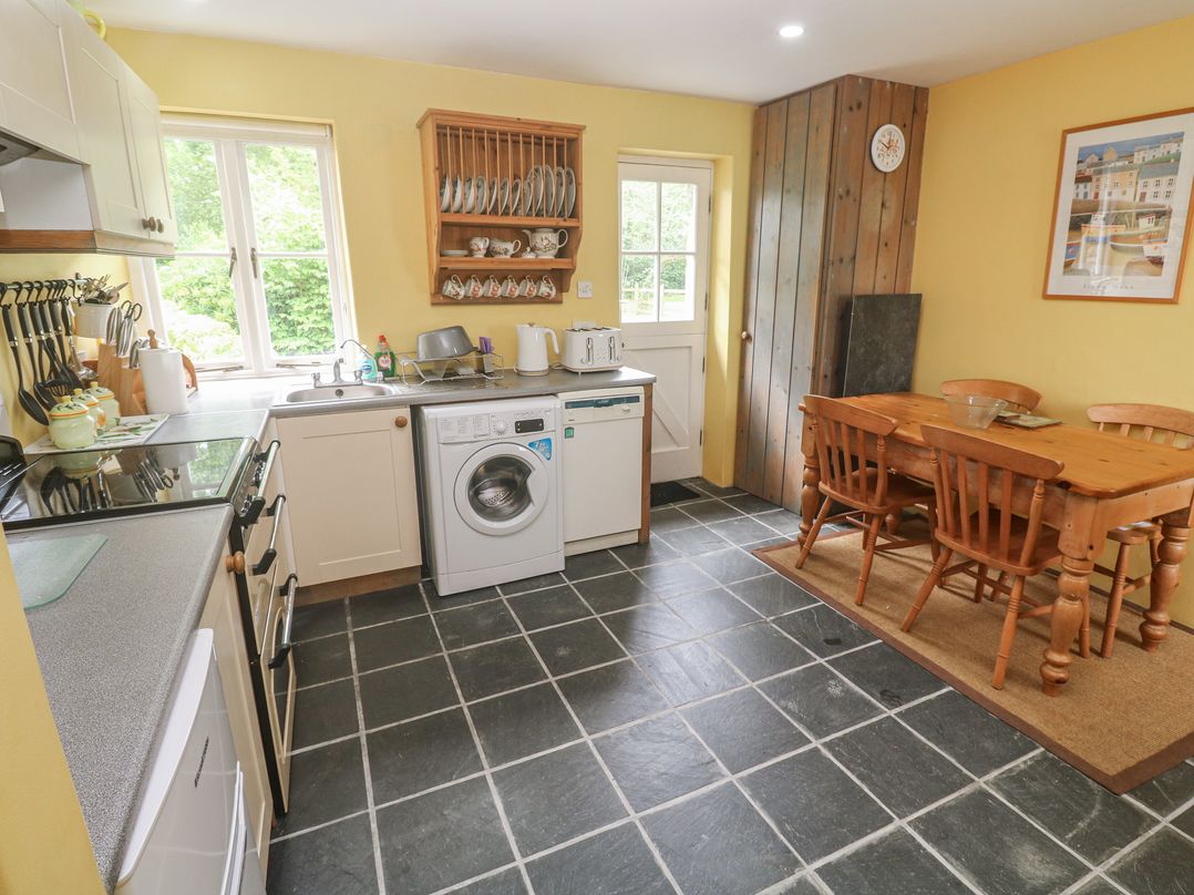 A kitchen with a washing machine and dining table at Swallows St Keverne, Lizard Peninsula