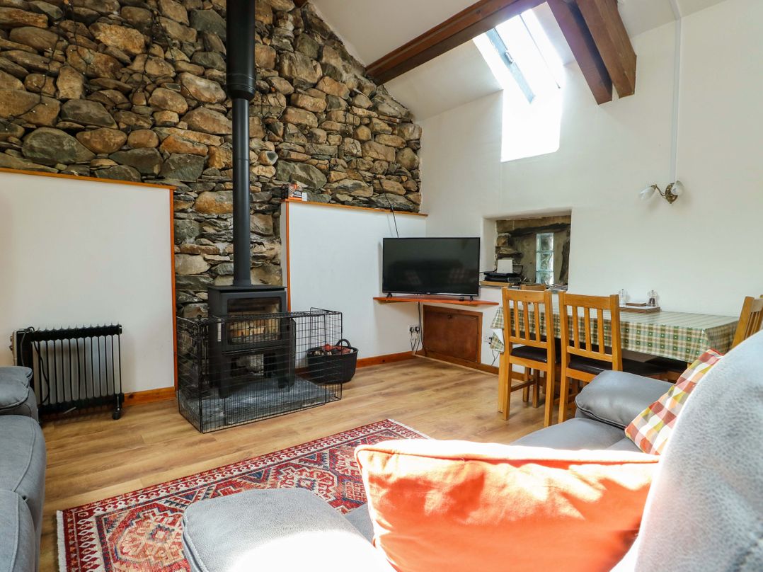 A living room with a wood stove, television, and dining table at Bythyn Ddol Hafod, Capel Curig