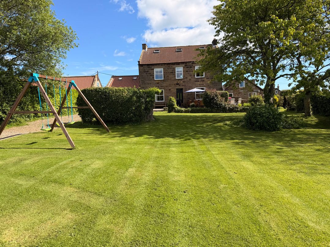 A garden with a swing set and a house at The Farmhouse in Boggle Hole near Robin Hood's Bay