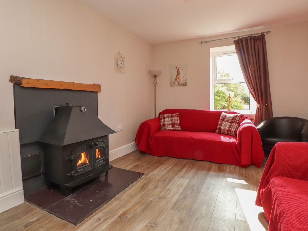 A living room with a fireplace and red sofa at The Farmhouse in Brynsiencyn near Newborough
