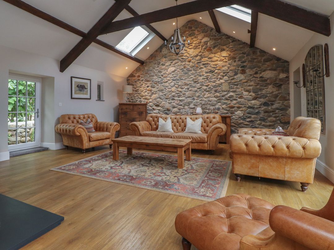 A living room with sofas, a table and a stone wall at Beudy'r Wennol in Groeslon