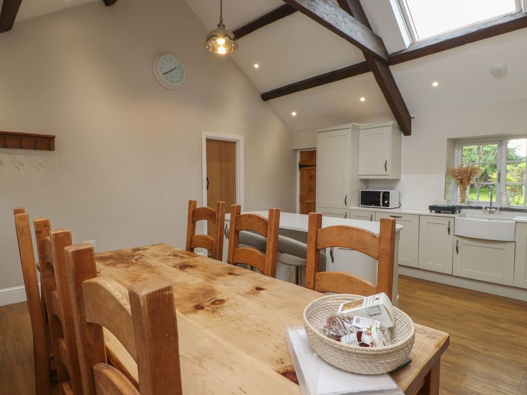 A dining room featuring a table with chairs and kitchen cabinets at Beudy'r Wennol Groeslon