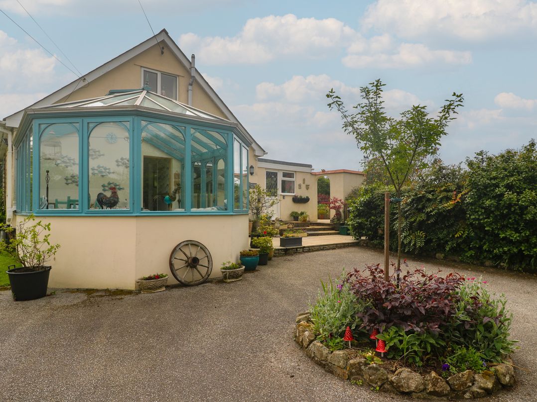 A conservatory next to a house with a flower bed and tree at Woolly Welcome in Goldsithney
