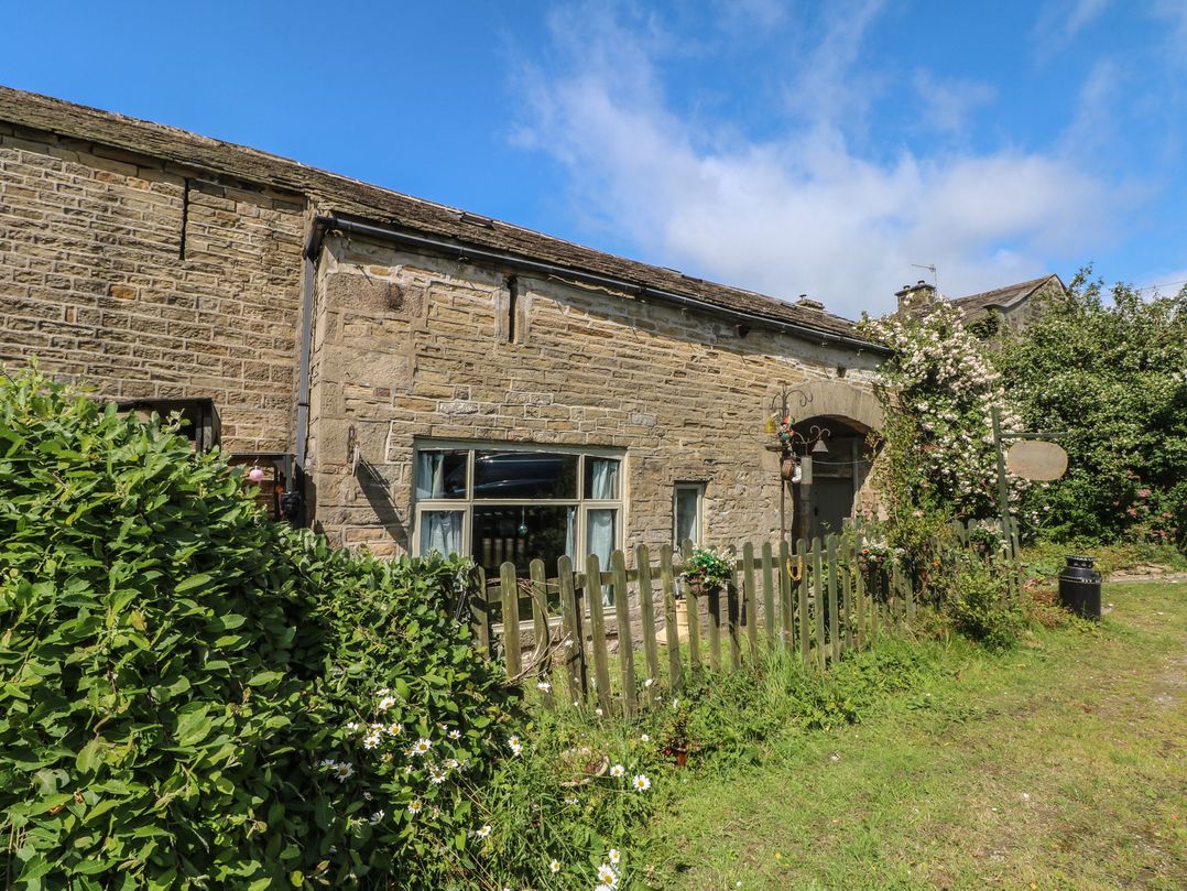 An exterior view of a stone building with a fence and plants at Moldy Warp Barn in Haworth
