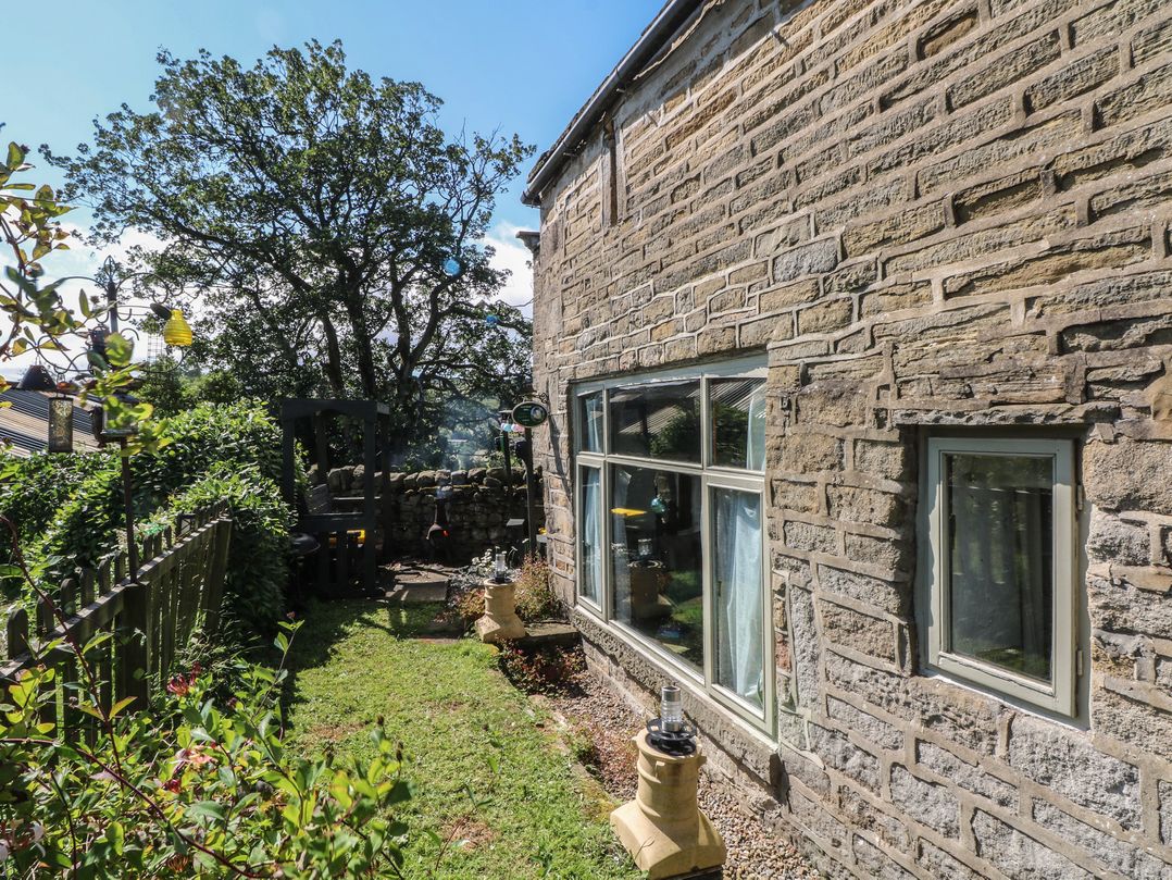 A garden with a stone wall and windows at Moldy Warp Barn in Haworth