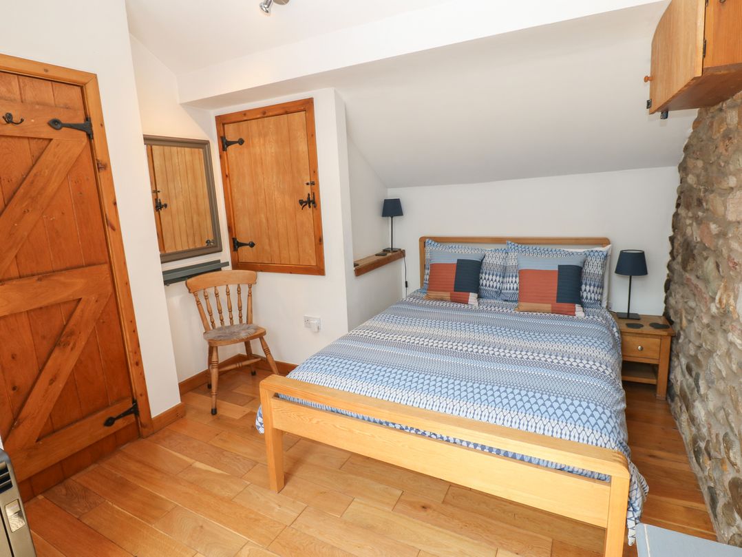 A bedroom with a bed, chair, and mirror at Chapel Cottage in Sandford, Cumbria