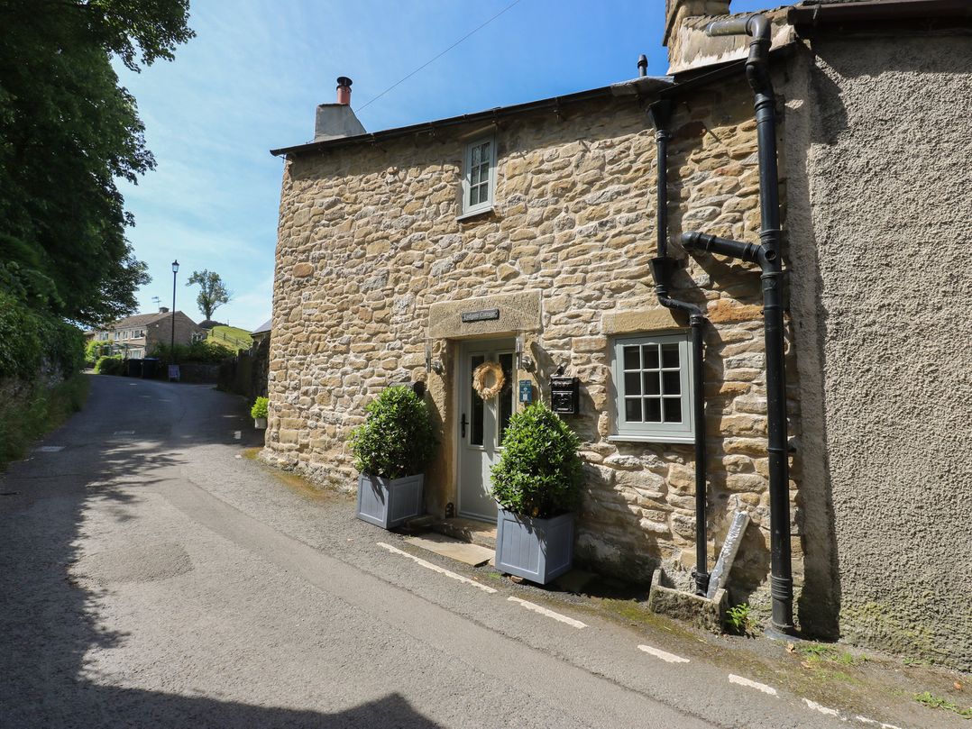 An outdoor view of a cottage with stone walls and plants at Lydgate Cottage in Eyam
