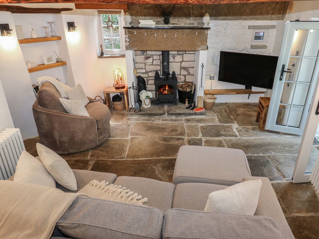 A living room with a fireplace and a television at Lydgate Cottage in Eyam