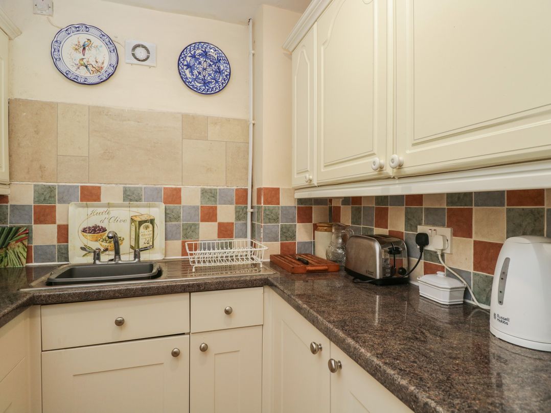 A kitchen with a sink, toaster, kettle, and decorative tiles at Dollar Ward House Basement Cirencester