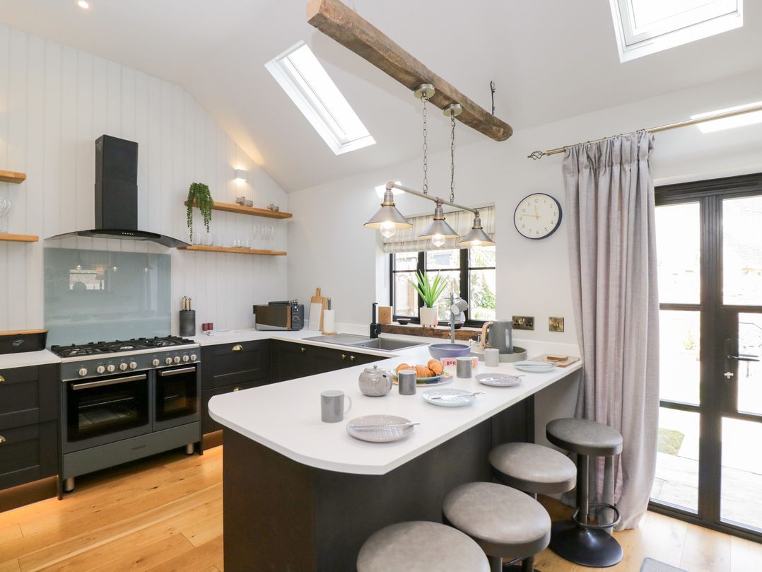 A kitchen with black cabinets white countertops bar stools and a clock on the wall at Millbank Cottage in Mickleton