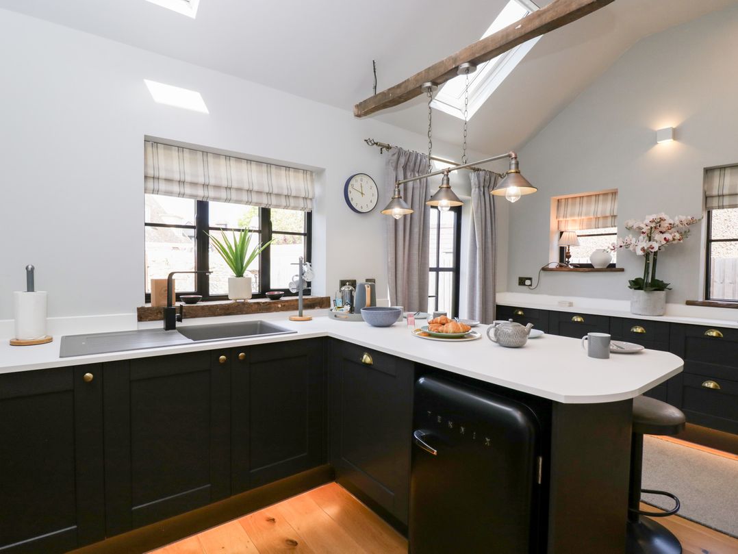 A modern kitchen with black cabinets white countertops a sink croissants on a plate and a hanging light fixture at Millbank Cottage in Mickleton