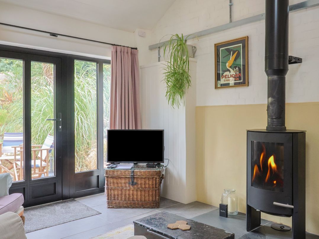 A living room with a television, wood stove, and basket at The Dairy in Bridport