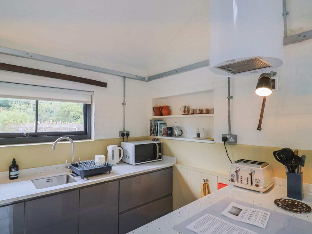 A kitchen with sink, microwave, toaster, and shelves at The Dairy in Bridport