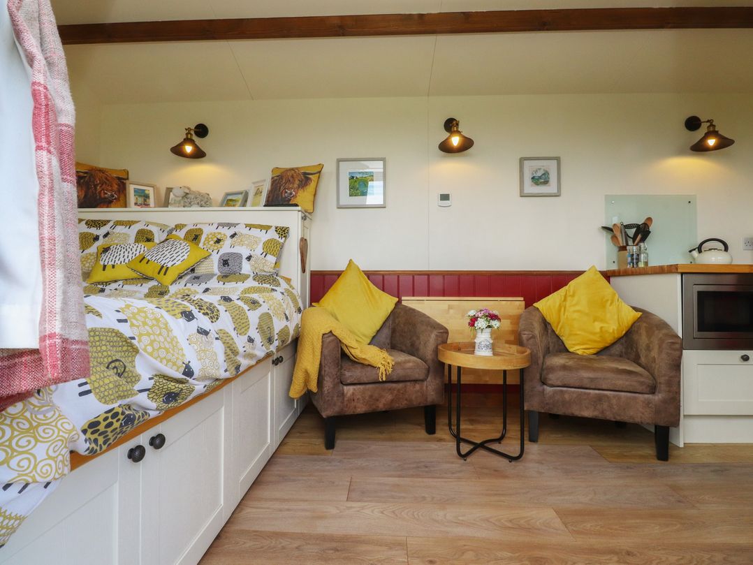 A living room with a bed, chairs, and table at The Herdsman Luxury Shepherds Hut in Barnoldswick