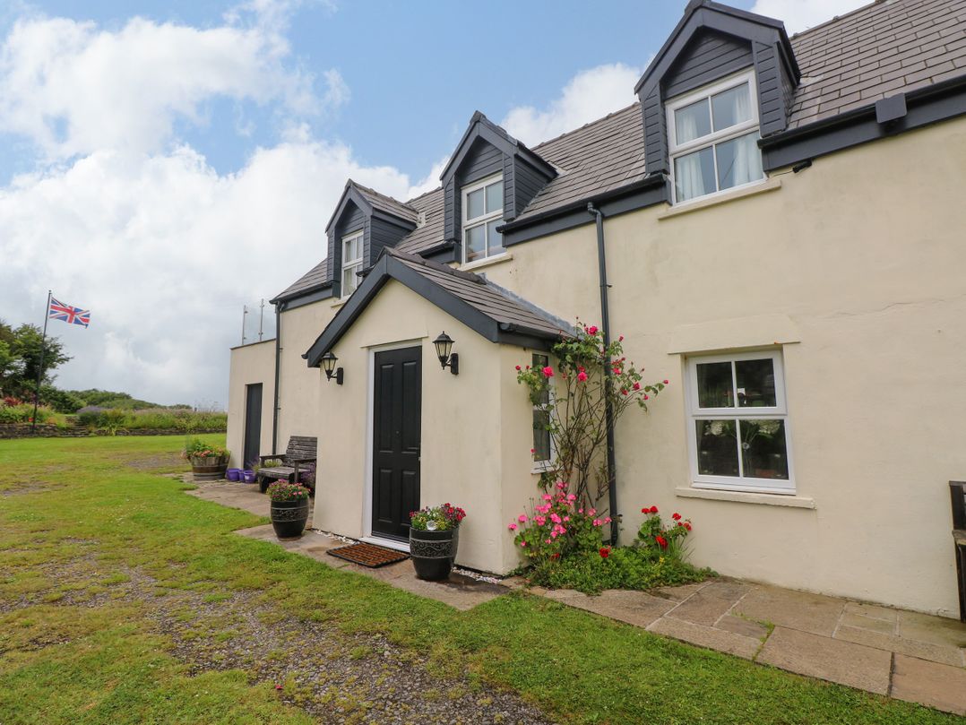 A house with a black door and flowers in planters at North Studdock Cottage, Angle near Pembroke