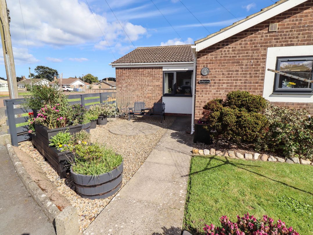 A garden with flower beds and seating at Flora Cottage Beadnell