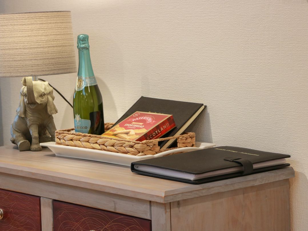 A table with a lamp, bottle, books, and a basket at Rosalin Cottage in Dreghorn near Irvine