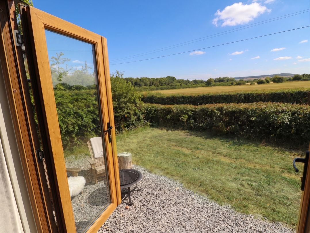 A view from an open door with a chair and table in the garden at Cariad Mawr Gwaenysgor near Prestatyn