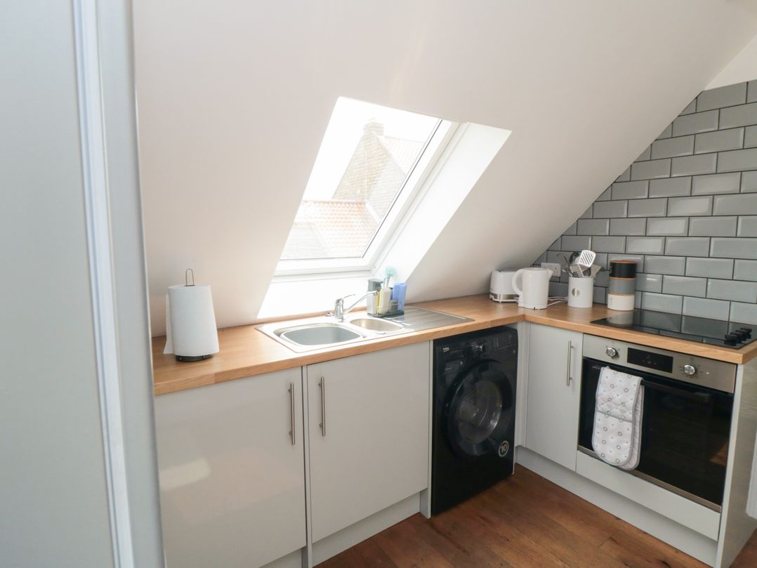 A kitchen with a sink under a skylight window a washing machine oven and kitchen utensils on a wooden countertop at Heron Nest in Cloughton near Scarborough