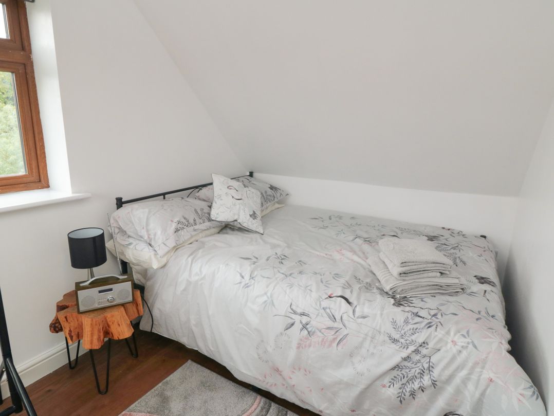 A bedroom with a bed covered in floral bedding a wooden bedside table with a lamp and radio at Heron Nest in Cloughton near Scarborough