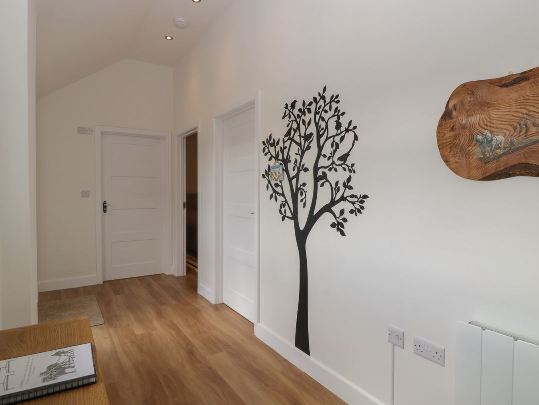 A hallway with wooden floor and white walls with black tree wall art and three white doors at Doubletree Cottage in Swainsford near Mere