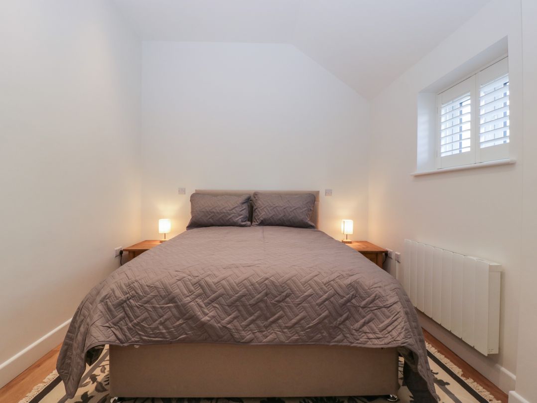 A bedroom with a double bed with two pillows and a quilt two bedside tables with lamps a small window with shutters and a radiator on the wall at Doubletree Cottage in Swainsford near Mere
