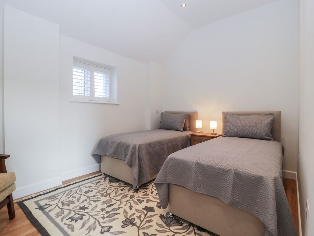 A bedroom with two single beds a small wooden nightstand with lamps and a patterned rug at Doubletree Cottage in Swainsford near Mere