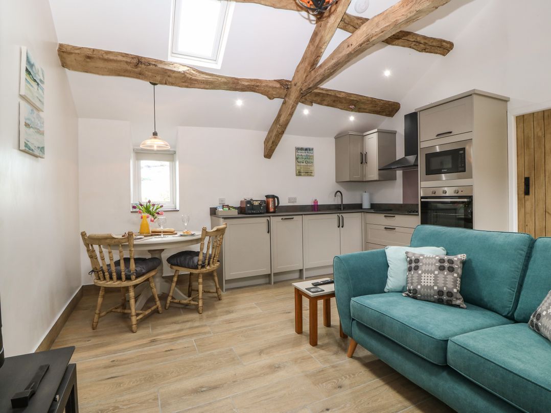 A kitchen and dining area with wooden beams on the ceiling a small round dining table with two chairs and a teal sofa at Y Stabl in Dyffryn Ardudwy